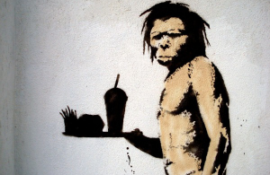 A Paleolithic Man holding a tray of fast food - Not Paleo Diet friendly